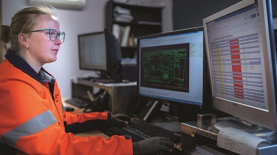 Direct Edge employee wearing orange high visibility jacket working at a computer with two screens.